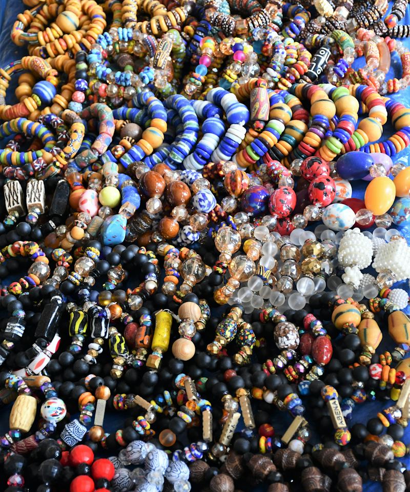 Hundreds of colourful handmade bead bracelets and necklaces laid out on a table for sale.